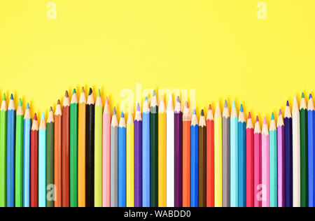 Colorful coloring pencils displayed in a wave on yellow background. Stock Photo
