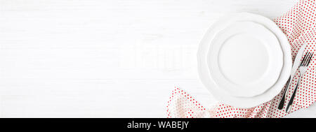 White empty plates and cutlery on polka dot napkin on white wooden table. Setting table top view. Banner for website. Stock Photo