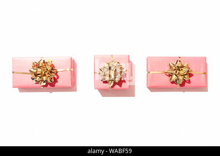 Line of three pink gift boxes on white table, minimal flat lay composition with copy space. Stock Photo