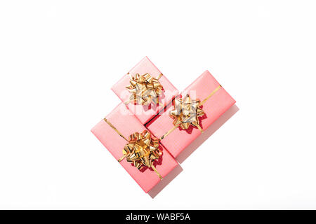 Three pink gift boxes with shiny golden bows on white background, overhead view. Stock Photo