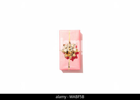 One rectangular pink gift box with golden bow in center of white background, top view. Stock Photo