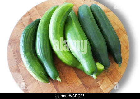 Overhead view of a group of cucumbers on a wooden chopping board isolated on a white background - John Gollop Stock Photo