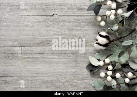 Side border of silver green leaves and white berries over a rustic gray wood background. Top view with copy space. Stock Photo