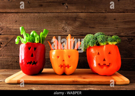 Healthy Halloween food. Vegetables for dipping in Jack o Lantern bell peppers. Side view against rustic wood. Stock Photo