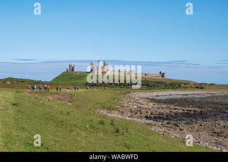 Walkers following a path towards Dunstanburgh Castle near Alnwick on the Northumberland coast, UK Stock Photo