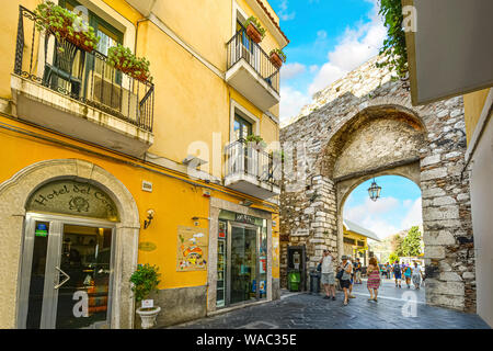 Tourists pass through the old stone city gate entrance in the picturesque town of Taormina on the island of Sicily in Italy Stock Photo