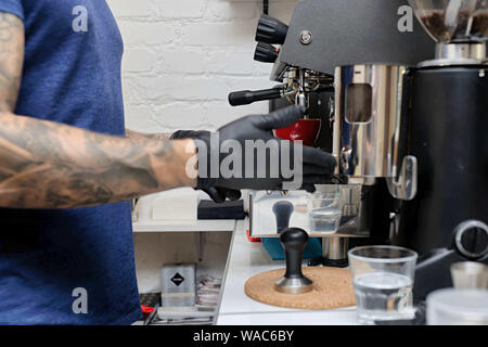 Hands of professional barista standing near the big metal coffee machine and looking how coffee pouring into the white cups Stock Photo