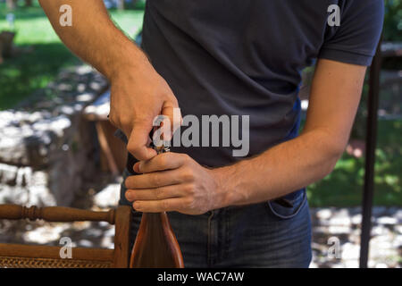 Man is blue tee-shirt is opening wine bottle. Celebration concept. Close-up Stock Photo
