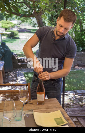 Man is blue tee-shirt is opening wine bottle. Celebration concept. Close-up Stock Photo