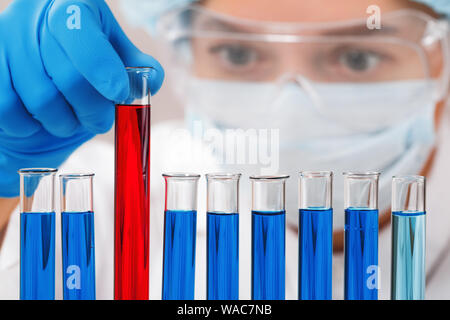 In a chemistry lab, a woman checks test tubes. Medical experiment. Chemist in safety glasses working on a test. Stock Photo