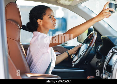 Side view of woman adjusting rear view mirror while driving a car Stock Photo