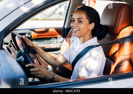 Smiling woman driving looking out a car window. Happy woman holding a steering wheel in the vehicle. Stock Photo
