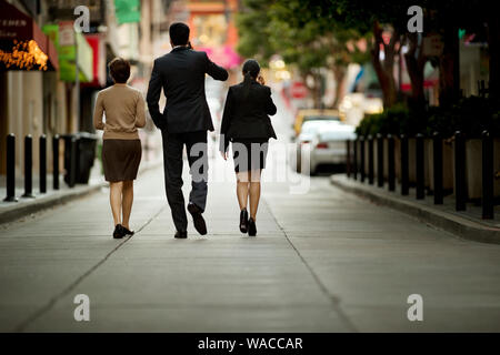 Three business colleagues talking while walking down an urban street. Stock Photo