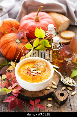 Bowl of pumpkin soup, fresh pumpkins and autumn leaves on rustic wooden background Stock Photo