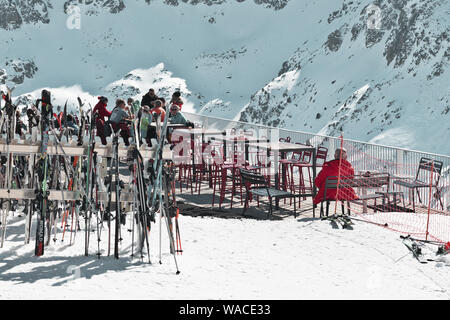 PYRENEES, ANDORRA - FEBRUARY 13, 2019: Unknown tourists at a ski resort in a cafe on the side of a mountain. Winter sunny day, outdoor chairs and tabl Stock Photo