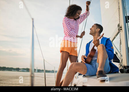 Happy young couple having fun playing the ukulele while sailing. Stock Photo