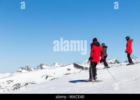 PYRENEES, ANDORRA - FEBRUARY 13, 2019: Three unknown skiers in red jackets on a mountainside. Sunny winter day, ski slope in the background Stock Photo
