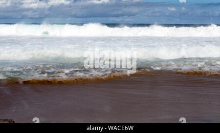 Tide is in. Vicious waves with the incoming tide crashing against the shoreline  with a very strong backwash. The surf is foamy on an overcast day. Stock Photo