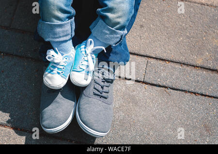 Children's feet in booties in the form of sneakers are on my father's feet. Dad walks with his little son. Paternity Stock Photo
