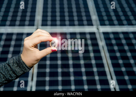 Selective focus on hand holding 1 euro coin and blurred solar panel cell on background with copy space. Money business in renewable energy power. Stock Photo