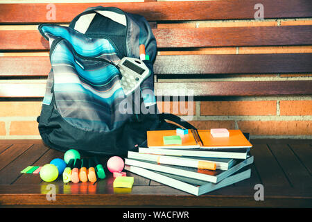 blue Backpack with multicolored school supplies on wooden bench Stock Photo