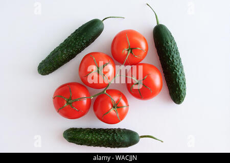 Five ripe red tomatoes on a branch and cucumbers on a white background. View from above. Stock Photo