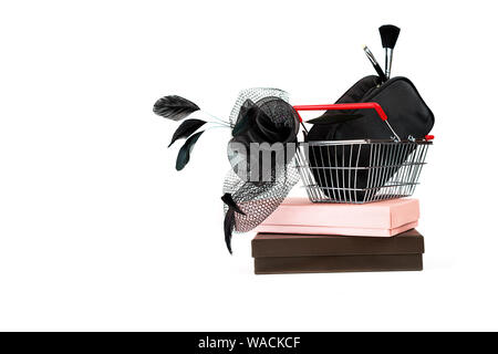 Shopping basket with black female hat with veil in retro style and bag with make up on gift boxes and white background. Stock Photo