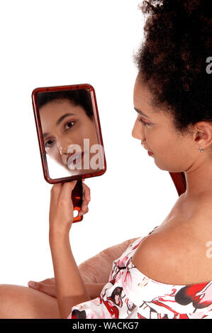 Lovely multi-racial woman looking at herself in a hand held mirror, sitting in a summer dress and curly black hair, isolated for white background Stock Photo