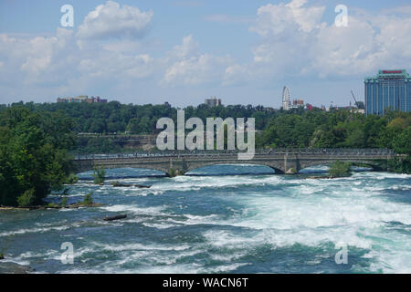 Niagara Falls, NY: Tourists on the Pedestrian Bridge to Goat Island, over the  American rapids. The Canadian side of the gorge is in the background. Stock Photo