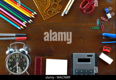 Colored pencils,pencils,scissor, rubber,sharpener, paperclip,rulers,pens,note blank paper,stapler calculator, and alarm clock on wooden table Stock Photo