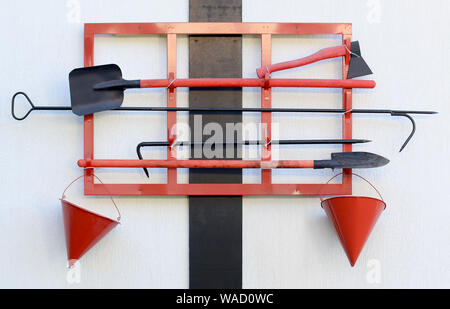 Wall-mounted fire shield open view. Fire extinguishing items. Tools. Shovel, hook, cone bucket, axe and other equipment hanged on fire point. Front Stock Photo