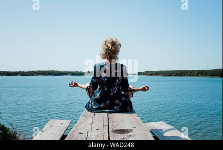 woman sat meditating outside looking at the sea on holiday Stock Photo