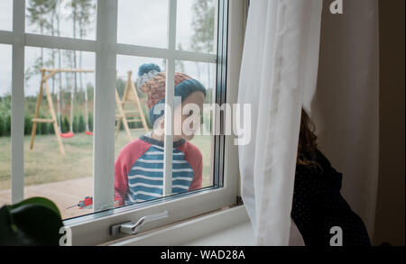 young boy looking through the window smiling at his sister Stock Photo