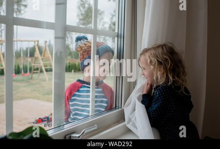 brother and sister looking through a window at each other playing Stock Photo