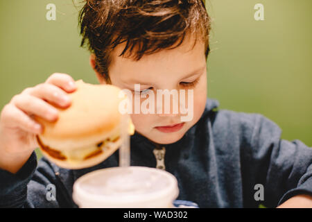 Boy holding burger while sitting at restaurant Stock Photo