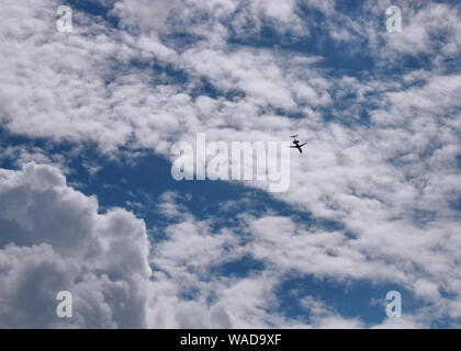 An airplane flies away from the camera through a cloudy blue sky. Stock Photo