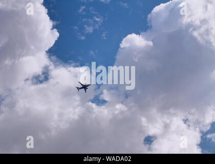 An airplane flies diagonally across a blue sky with puffy white clouds. Stock Photo