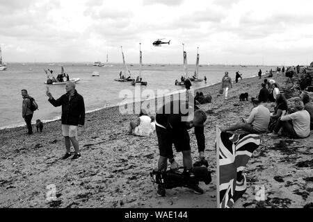 Crowds of spectators watching Cowes Week yacht racing from the beach at Cowes seafront on the Isle of Wight Stock Photo