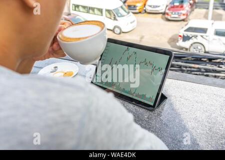 Rear view of Asian businessman drinking cappuccino and using tablet Stock Photo