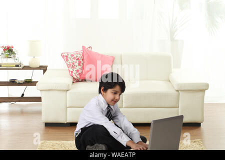 Schoolboy sitting on floor and using laptop Stock Photo