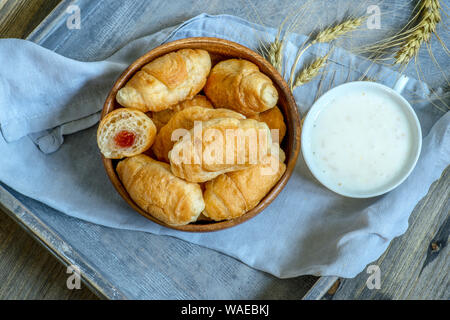 Croissants, a cup with kefir and ears of grain on a wooden tray. The concept of a wholesome breakfast Stock Photo