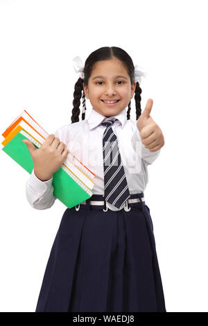 Schoolgirl standing with books and showing thumbs up sign Stock Photo