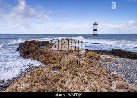 Lighthouse at Penmon Point, Anglesey, North Wales on a windy day with waves breaking on the foreshore Stock Photo