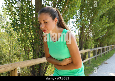 Woman has side cramp. Young woman suffering from abdominal pain while running outdoor. Stock Photo