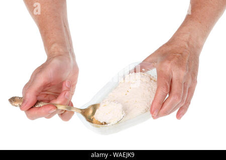 An senior  elderly woman takes fresh cottage cheese with a spoon from a  plastic pack. Isolated on white studio closeup Stock Photo
