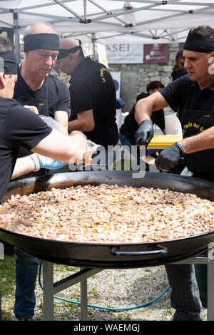 RASSA, ITALY - AUGUST 2019 - Men preparing paella in a big paellera, putting ingredients inside the pan. Rassa blueberry festival, Italy. Vertical sho Stock Photo