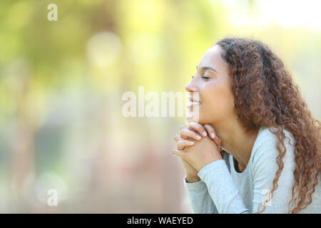 Side view portrait of a happy mixed race woman meditating and breathing fresh air outdoors in a park Stock Photo