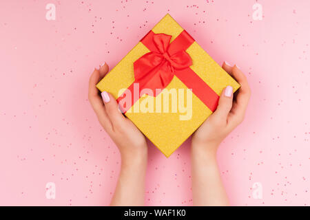 Female hands with christmas gift box with bow on pink sparkles background. Stock Photo