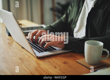 Man typing on laptop computer keyboard at table Stock Photo