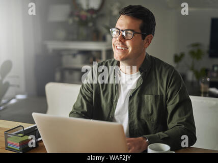 Smiling man with laptop sitting at desk looking away Stock Photo